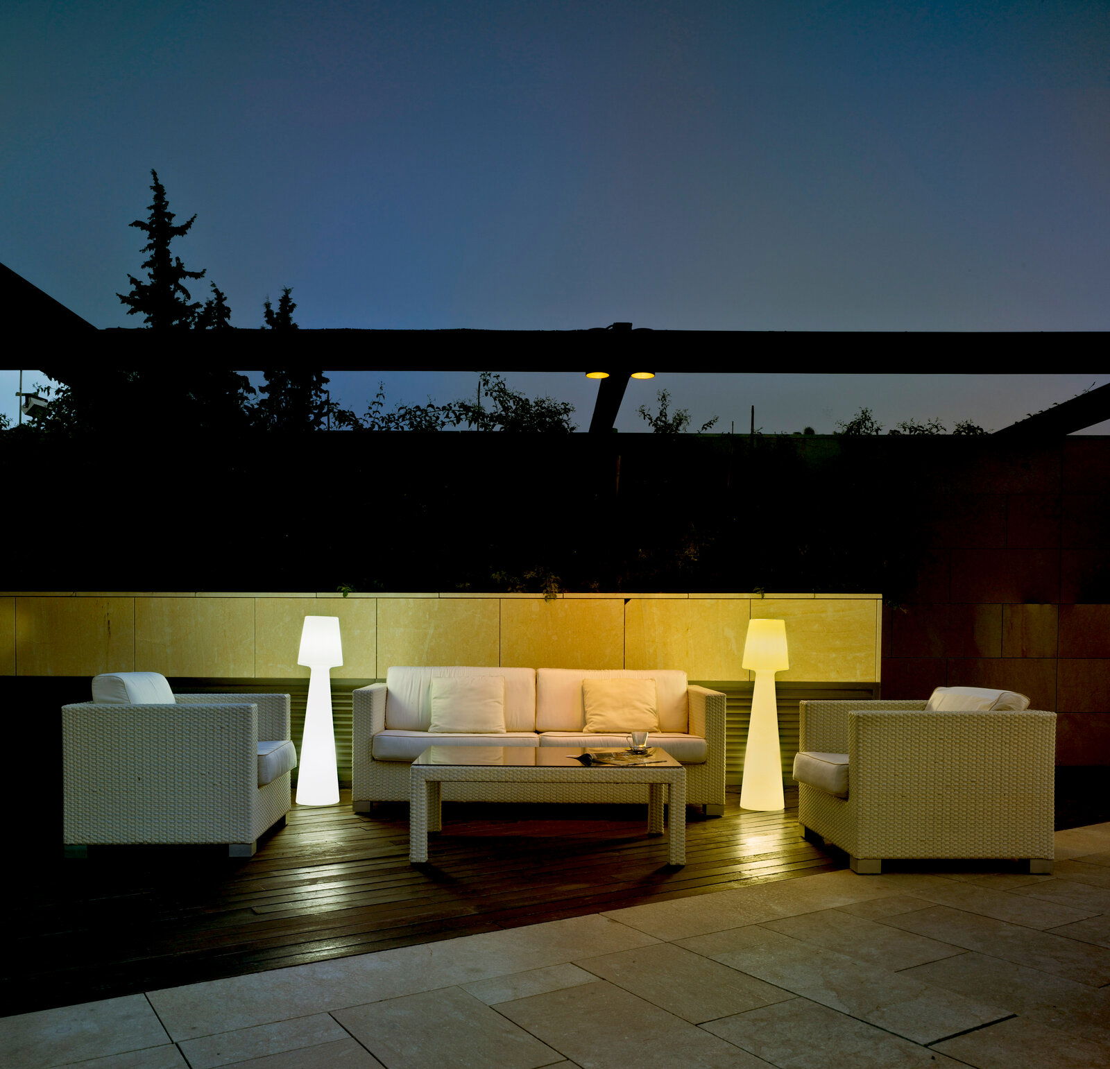 Newgarden LED-Stehleuchte LOLA Stehleuchte LOLA 110 in einem modernen Außenbereich, umgeben von weißen Rattanmöbeln, bei Dämmerung beleuchtet.