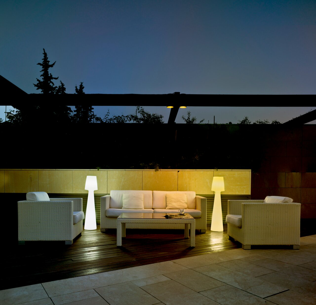 Stehleuchte LOLA 110 in einem modernen Außenbereich, umgeben von weißen Rattanmöbeln, bei Dämmerung beleuchtet.