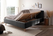 Seitliche Perspektive auf ein Polsterbett mit hochgeklappter Matratze, das Stauraum darunter zeigt. Das Bett steht in einem hellen Raum mit moderner Dekoration.