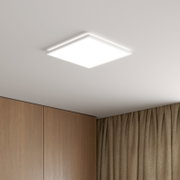 Quadratische, flache LED-Deckenleuchte in Weiß mit diffuser Lichtfläche, an der Zimmerdecke montiert; Ansicht schräg von unten in einer Raumecke mit Holzschrank und Vorhängen