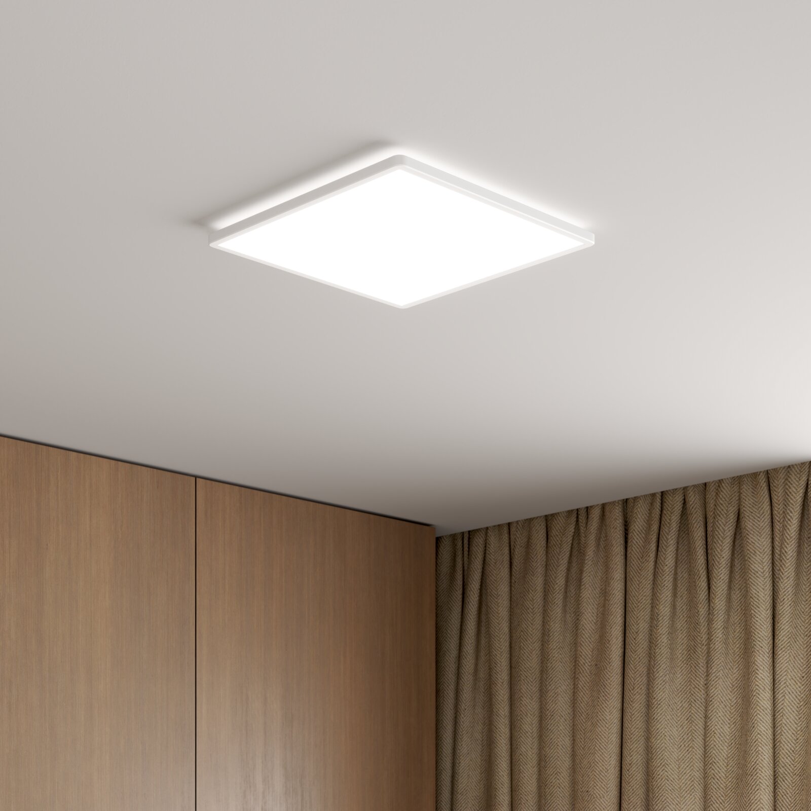 Quadratische, flache LED-Deckenleuchte in Weiß mit diffuser Lichtfläche, an der Zimmerdecke montiert; Ansicht schräg von unten in einer Raumecke mit Holzschrank und Vorhängen