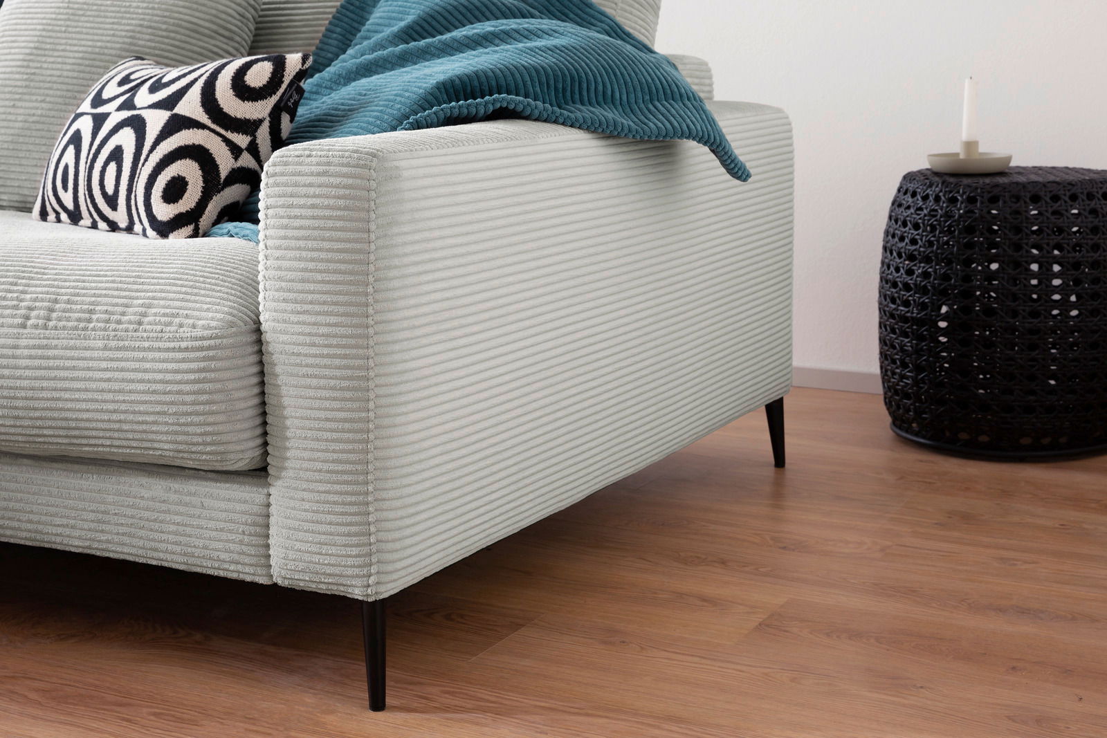 Nahaufnahme einer Longchairkombination mit hellgrauem, geripptem Stoffbezug, schwarzem Beistelltisch und dekorativem Kissen, seitliche Perspektive.