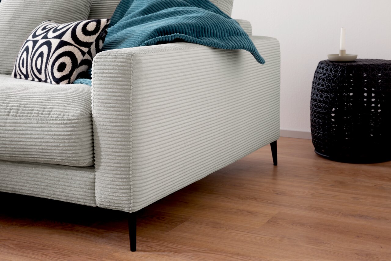 Nahaufnahme einer Longchairkombination mit hellgrauem, geripptem Stoffbezug, schwarzem Beistelltisch und dekorativem Kissen, seitliche Perspektive.