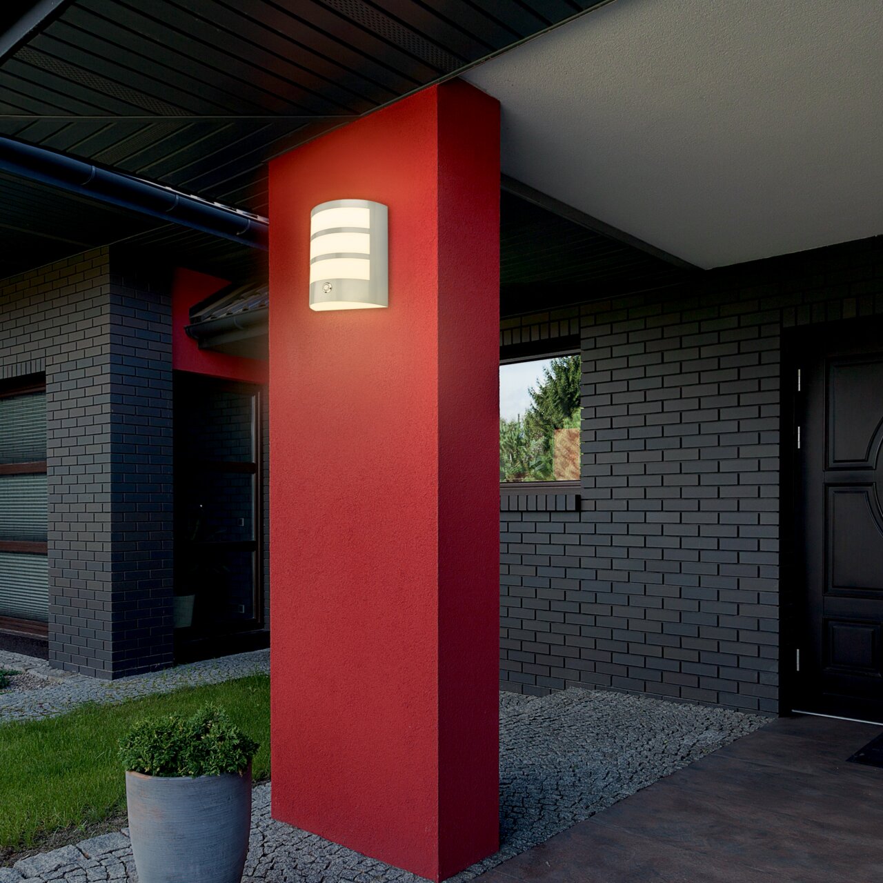Moderne Akku-Außenwandleuchte an einer roten Wand, seitliche Perspektive