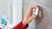 Nahaufnahme einer Hand, die einen tesa Powerstrip Waterproof Haken an einer Badezimmerwand anbringt.