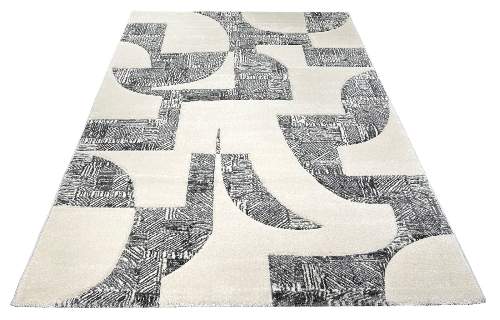 Moderner Teppich in Creme und Grau mit abstraktem geometrischem Muster, schräg von oben in Perspektive fotografiert
