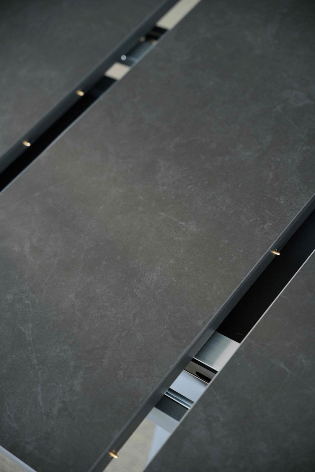 Nahaufnahme eines Esstisches mit dunkler, steinartiger Oberfläche und sichtbarem Verlängerungsmechanismus.