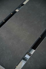 Nahaufnahme eines Esstisches mit dunkler, steinartiger Oberfläche und sichtbarem Verlängerungsmechanismus.