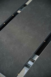 Nahaufnahme eines Esstisches mit dunkler, steinartiger Oberfläche und sichtbarem Verlängerungsmechanismus.