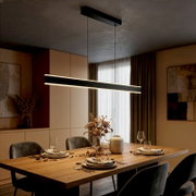 Moderne, schwarze LED-Pendelleuchte in schlanker Balkenform über einem gedeckten Holzesstisch, warmweiß leuchtend, fotografiert in leicht seitlicher Perspektive von schräg unten im Esszimmer