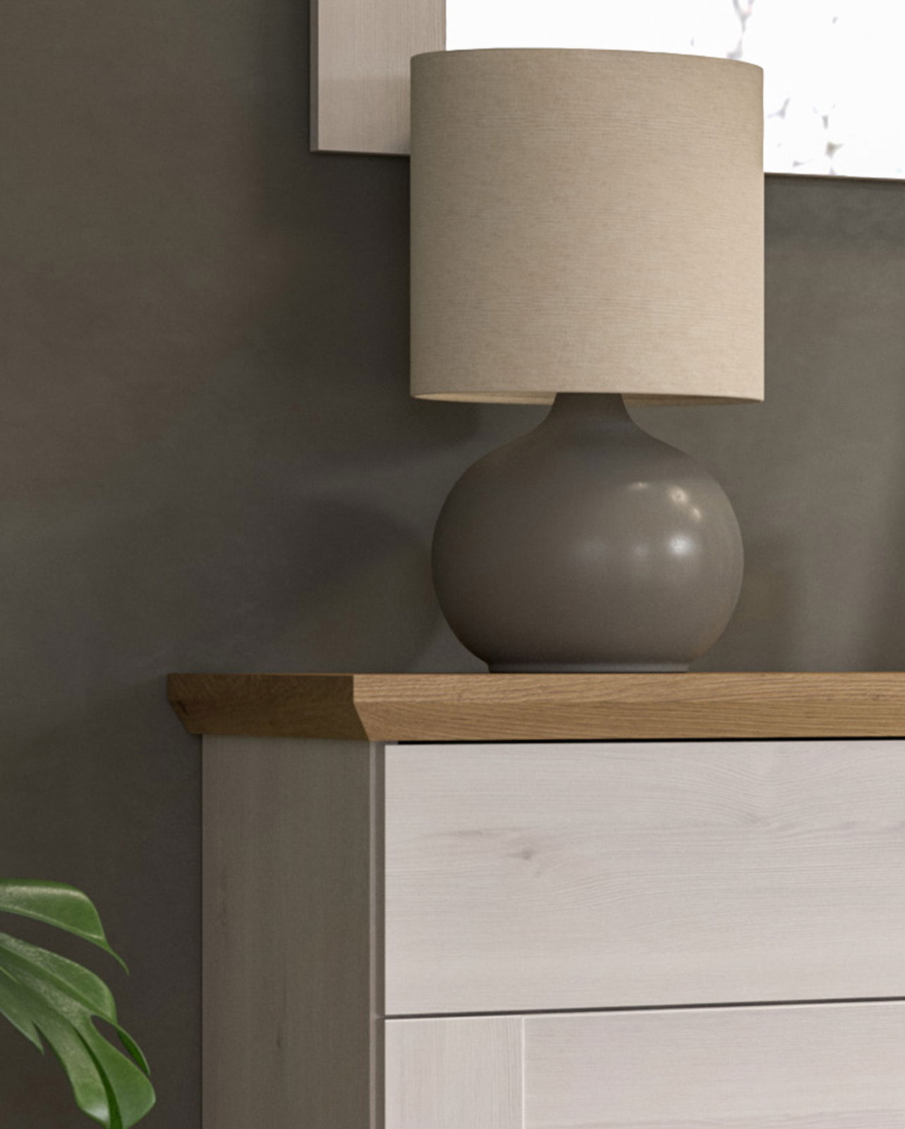 Nahaufnahme einer modernen Tischlampe mit rundem, grauem Sockel und beigem Lampenschirm auf einer Holzkommode.