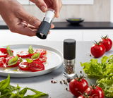 Salz- und Pfeffermühle TUSOME in moderner Küche, eine Hand streut Salz auf Tomatensalat, seitliche Perspektive