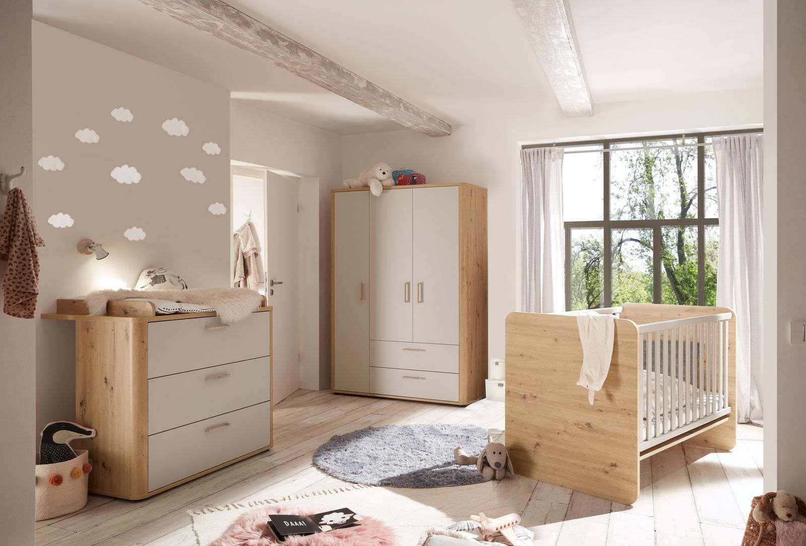 Gemütliches Babyzimmer mit Holzmöbeln, bestehend aus einem Kleiderschrank, einer Wickelkommode und einem Babybett, aus der Perspektive von der Zimmertür aus gesehen.