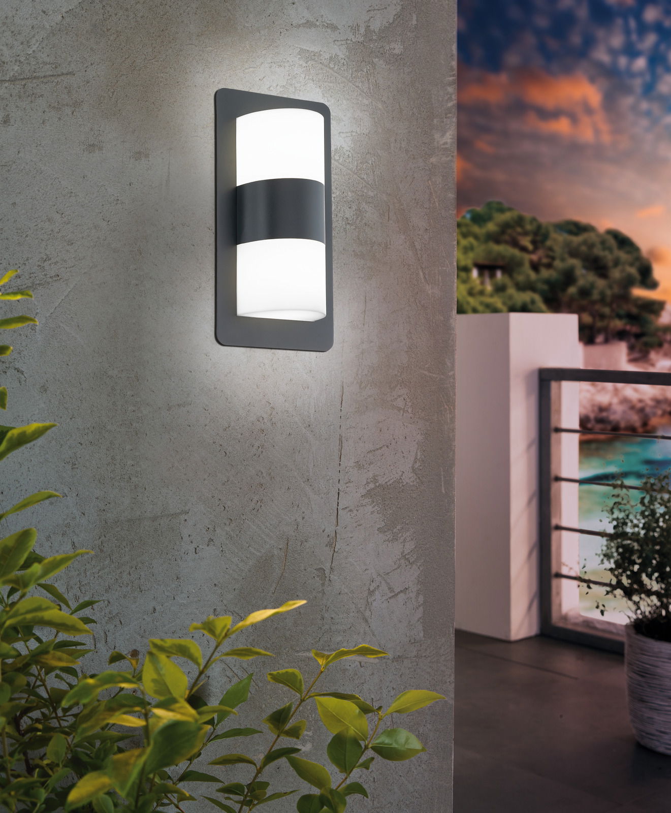 Moderne Wandleuchte 'CISTIERNA' an einer Betonwand, seitliche Perspektive, mit Blick auf einen Balkon bei Sonnenuntergang.