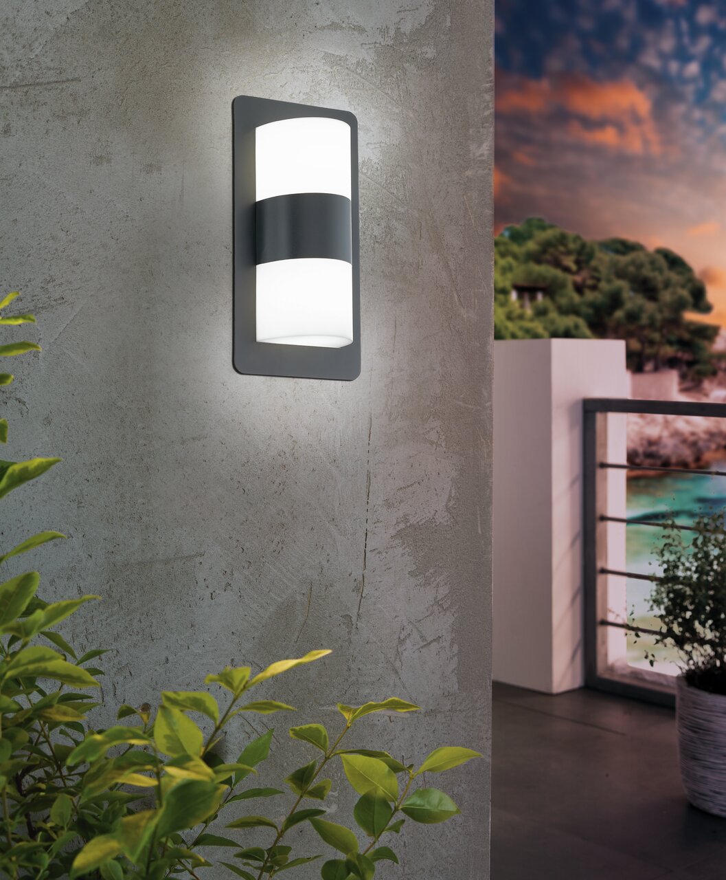 Moderne wandlamp 'CISTIERNA' aan een betonnen muur, zijaanzicht, met uitzicht op een balkon bij zonsondergang.