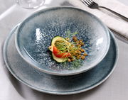 Nahaufnahme eines stilvollen, blauen Tellersets mit 18 Teilen, präsentiert mit einer eleganten Speiseanrichtung aus Linsen, Tomate und Gurke.