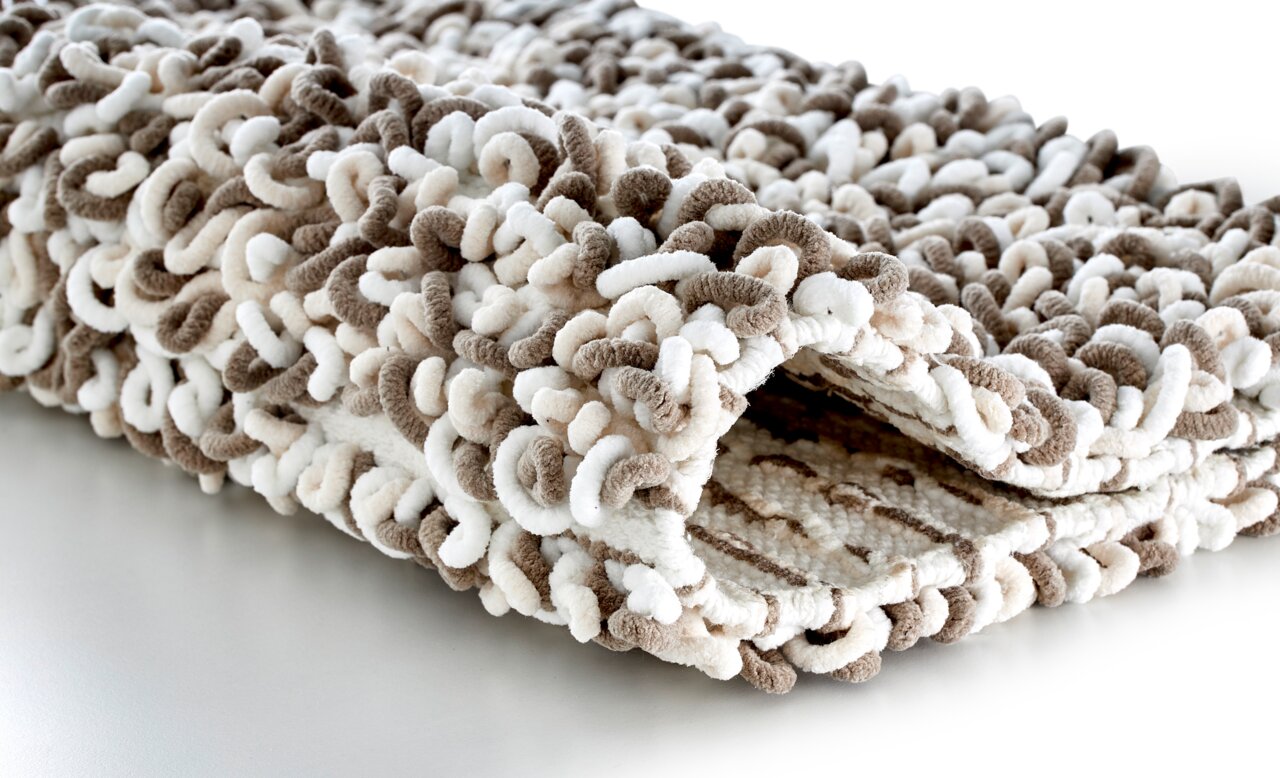 Nahaufnahme eines beigen und weißen Badteppichs mit weicher, strukturierter Oberfläche, seitliche Perspektive.