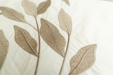 Nahaufnahme von Bettwäsche mit gesticktem Blattmuster in Beige auf weißem Hintergrund, von oben betrachtet.