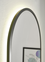 Nahaufnahme eines ovalen Spiegels mit schwarzem Rahmen und Hintergrundbeleuchtung, seitliche Perspektive