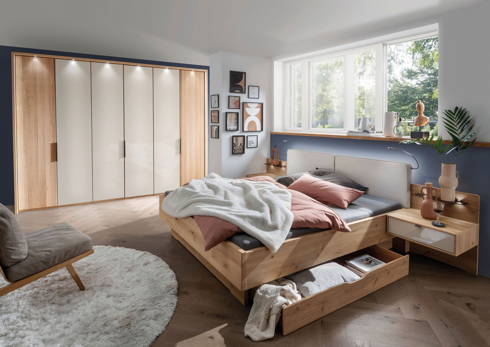 Gemütliches Schlafzimmer mit einem großen Holzbett, das über einen geräumigen Bettschubkasten verfügt. Der Raum ist modern eingerichtet mit einem großen Kleiderschrank und dekorativen Elementen. Perspektive von der Seite des Bettes.
