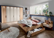 Gezellige slaapkamer met een groot houten bed, voorzien van een ruime opberglade. De kamer is modern ingericht met een grote kledingkast en decoratieve elementen. Aanzicht vanaf de zijkant van het bed.