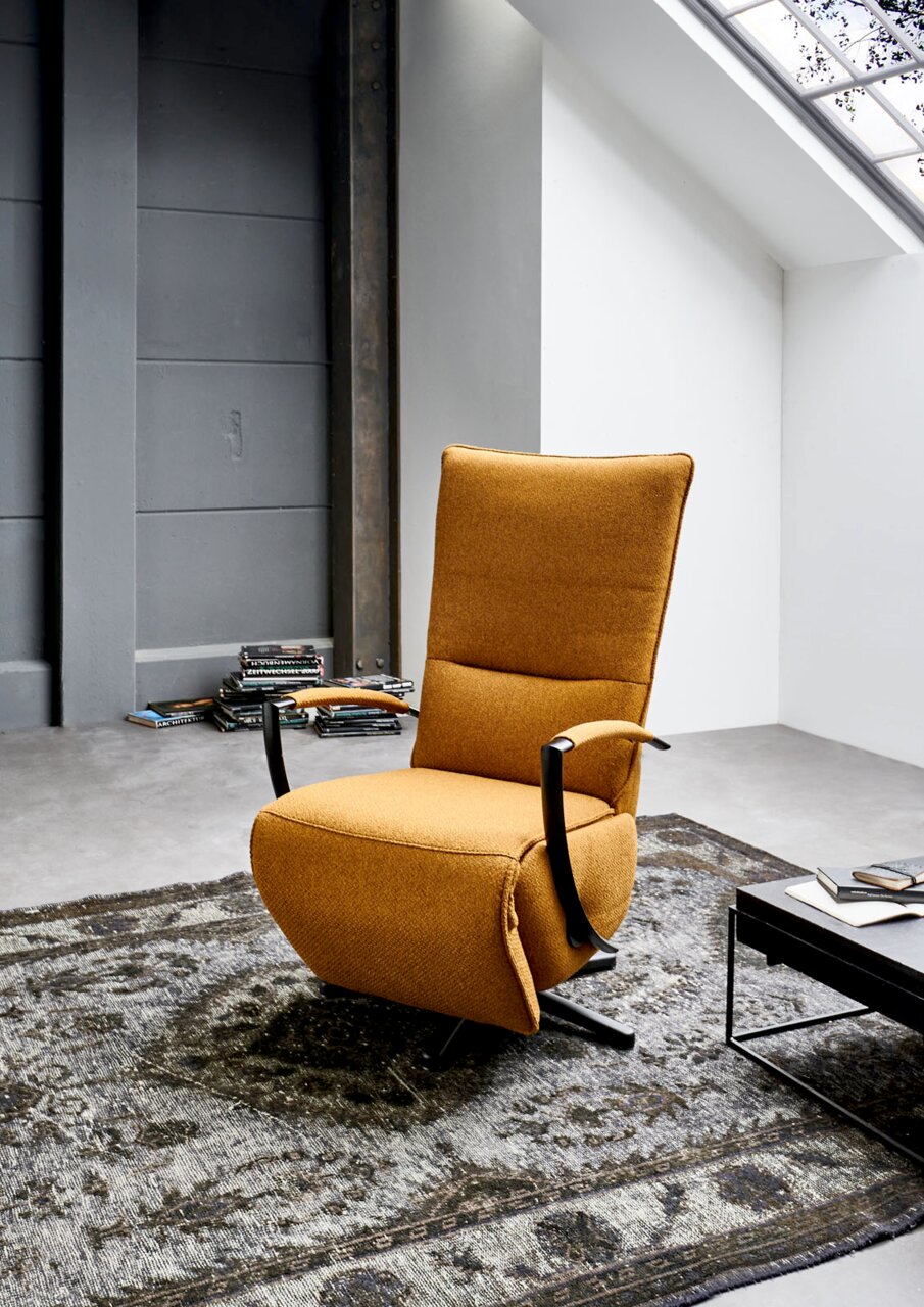 Moderne, draaibare relaxfauteuil in mosterdgeel, gezien vanaf de zijkant, geplaatst op een tapijt met patroon in een stijlvolle ruimte.