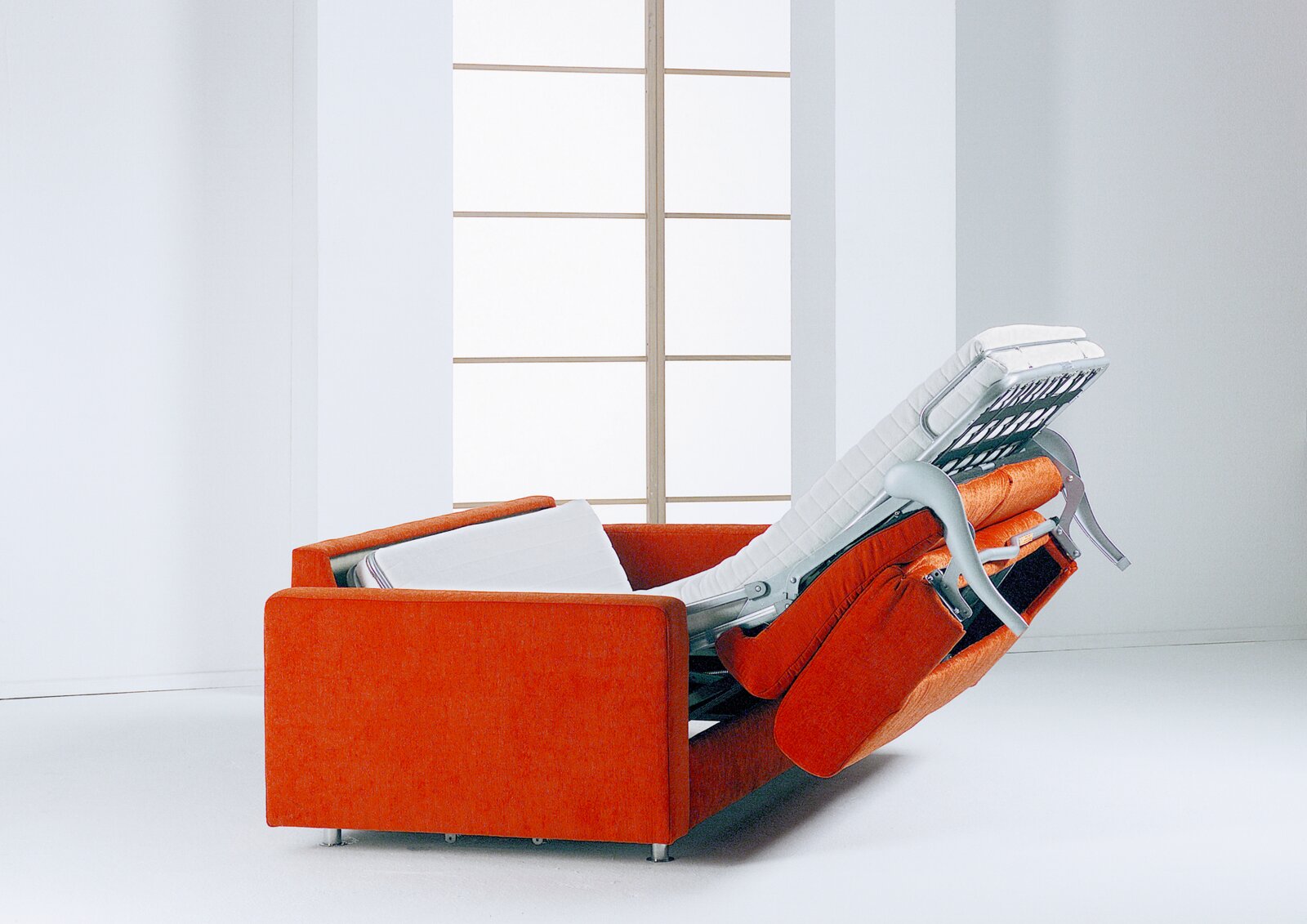 Orangefarbenes Schlafsofa mit ausgeklapptem Bettmechanismus und weißer Matratze, aus seitlicher Rückansicht in einem hellen Raum gezeigt