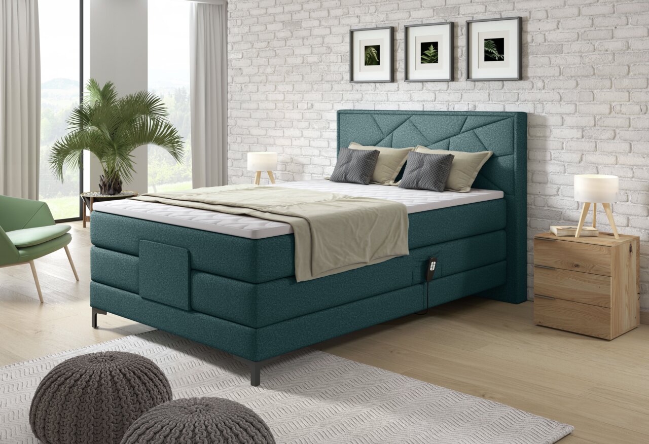 Boxspringbett in modernem Schlafzimmer, seitliche Perspektive, mit grüner Polsterung, Kissen und Decke, umgeben von Pflanzen und Holzmöbeln.