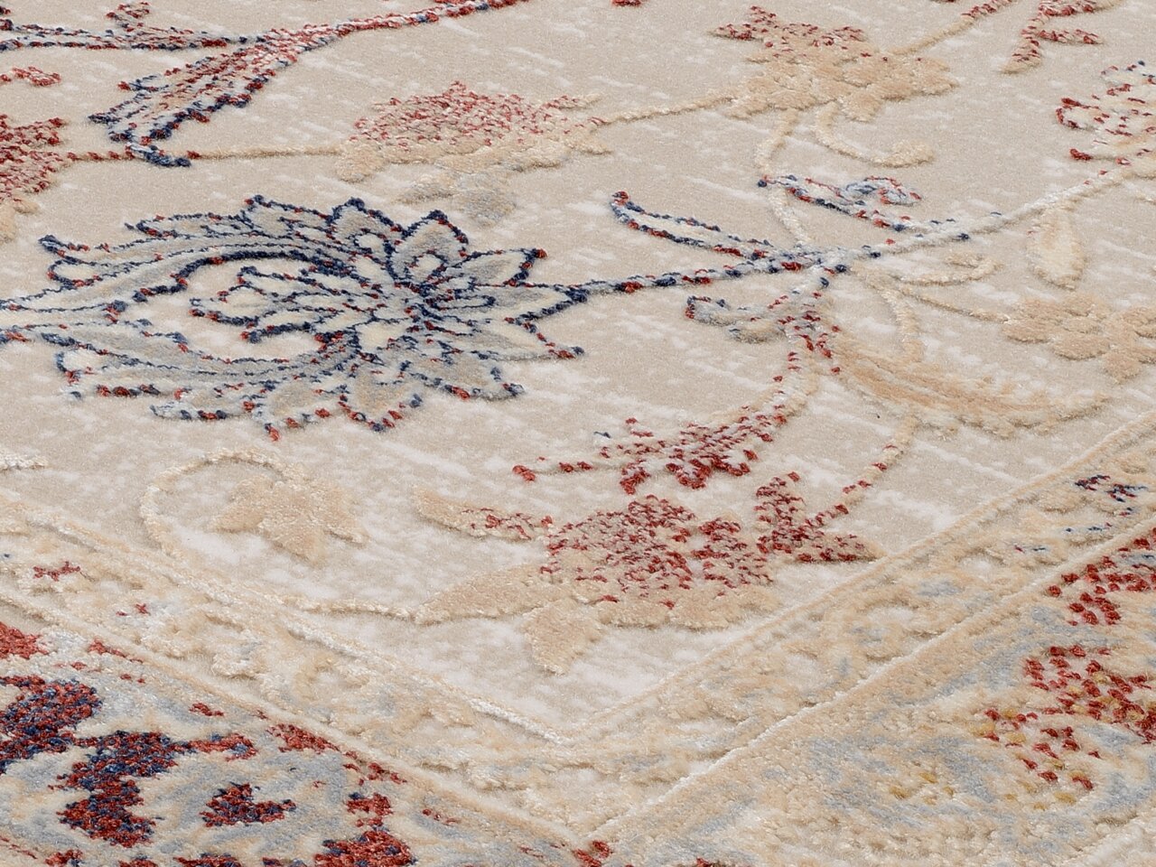 Nahaufnahme eines Orientteppichs mit floralen Mustern in Blau, Rot und Beige, perspektivisch von der Seite aufgenommen.
