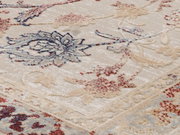 Nahaufnahme eines Orientteppichs mit floralen Mustern in Blau, Rot und Beige, perspektivisch von der Seite aufgenommen.