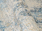 Nahaufnahme eines Designer-Teppichs mit abstraktem Muster in Blau-, Grau- und Beigetönen, leicht aufgerollt.