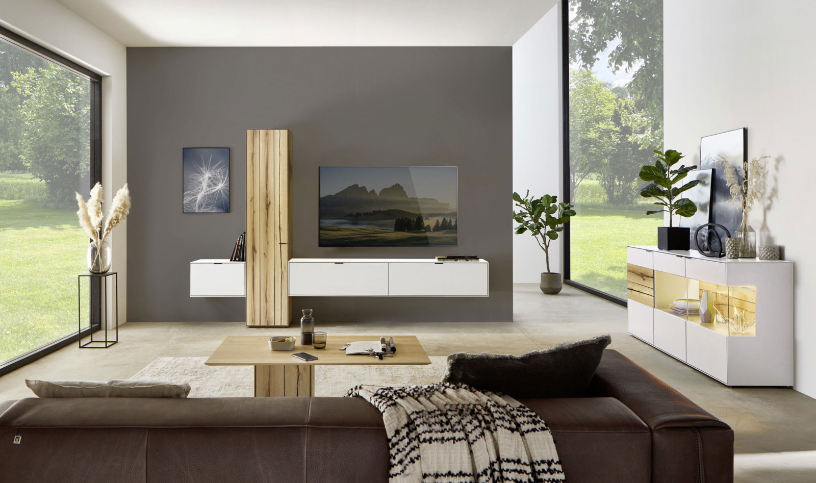Moderne Wohnzimmeransicht mit Wandkombination, bestehend aus weißen Schränken und Holzelementen, im Vordergrund ein braunes Sofa, seitliche Perspektive.