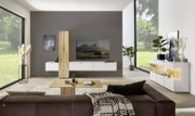 Moderne Wohnzimmeransicht mit Wandkombination, bestehend aus weißen Schränken und Holzelementen, im Vordergrund ein braunes Sofa, seitliche Perspektive.
