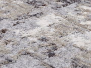 Nahaufnahme eines Designer-Teppichs mit weicher, flauschiger Textur in verschiedenen Grautönen und Beige, von oben betrachtet.