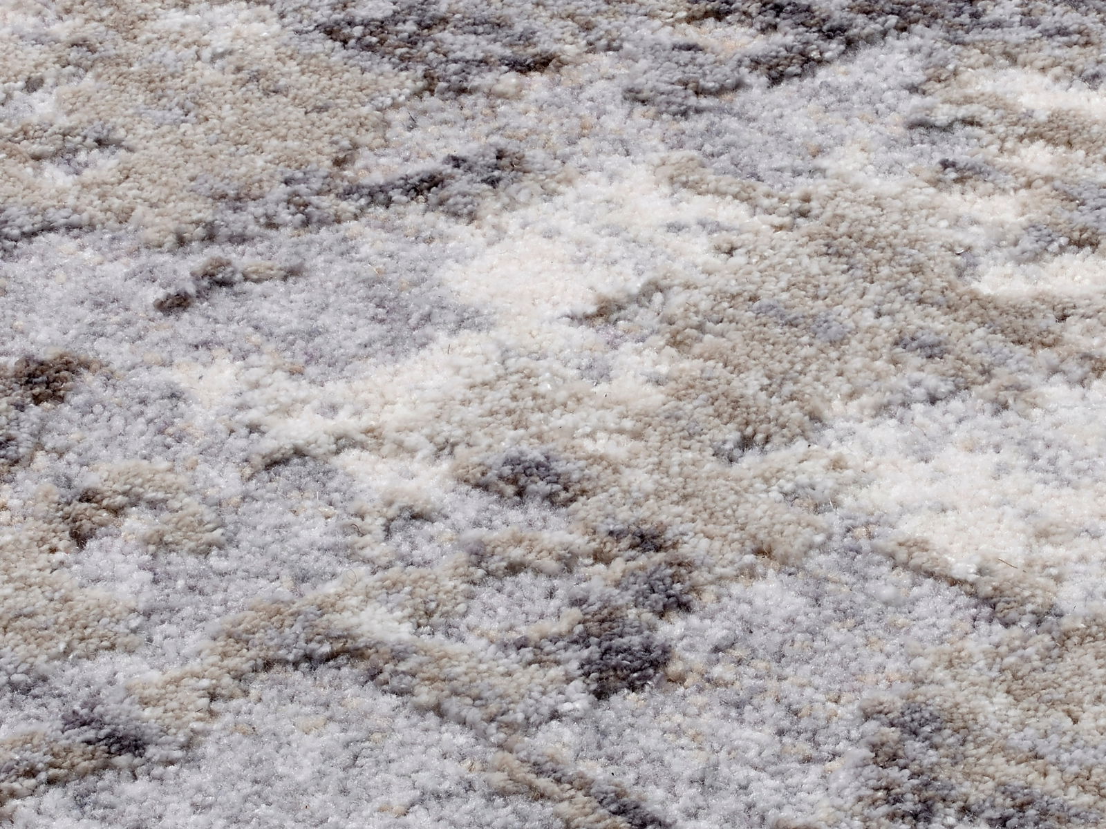 Nahaufnahme eines Designer-Teppichs mit weicher, flauschiger Textur in verschiedenen Grautönen und Beige, von oben betrachtet.