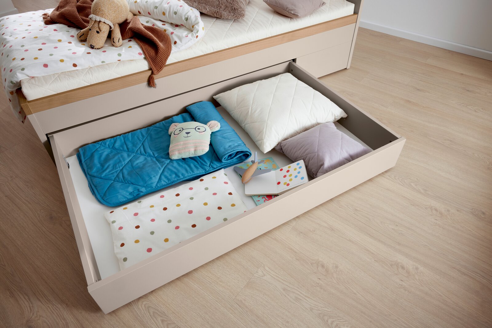 Bettkasten mit geöffnetem Schubfach, gefüllt mit Kissen, Decken und Spielzeug, aus der Vogelperspektive fotografiert.