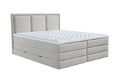 Lichtgrijs gestoffeerd tweepersoons boxspringbed met hoge, verticaal verdeeld hoofdbord en witte gewatteerde topper, schuin van voren gezien