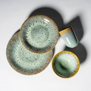 Keramik-Geschirrset mit zwei Tellern, Schale und Becher in blau-grüner Effektglasur mit braunem Rand auf weißem Hintergrund, Draufsicht von oben