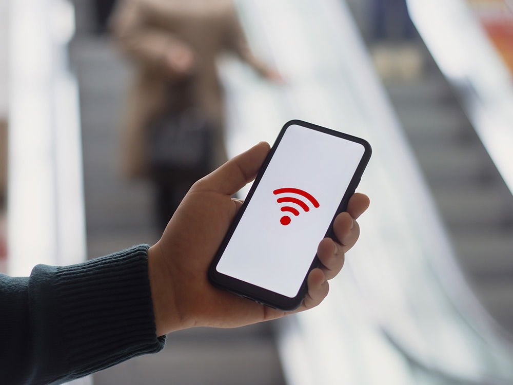 Hand hält Smartphone mit WiFi-Symbol auf dem Bildschirm in einer städtischen Umgebung.