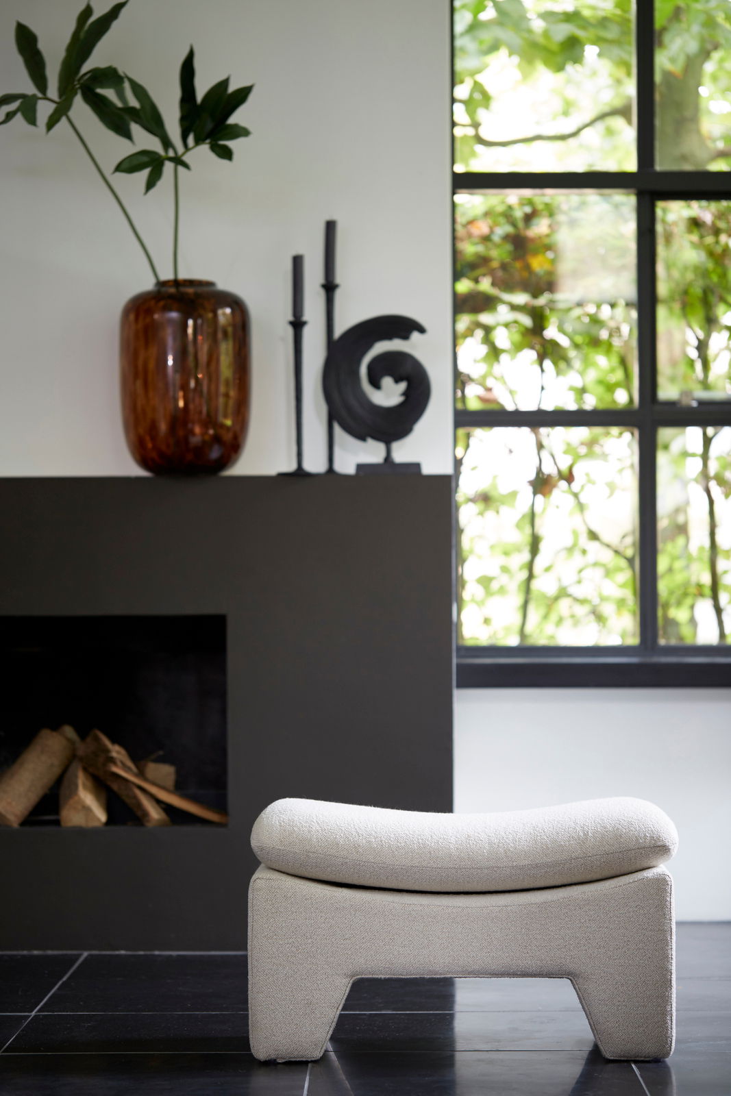 Light&Living Sitzpuff DASHA Moderner Sitzpuff in heller Farbe, frontal vor einem Kamin und einem Fenster mit Blick ins Grüne.