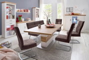 Modernes Esszimmer-Set mit rechteckigem Holztisch in Weiß/Eiche und vier braunen Freischwinger-Stühlen, umgeben von weißen Vitrinen und Sideboards mit Holzoberflächen; Perspektive: schräger Frontblick auf Tisch und Stühle.