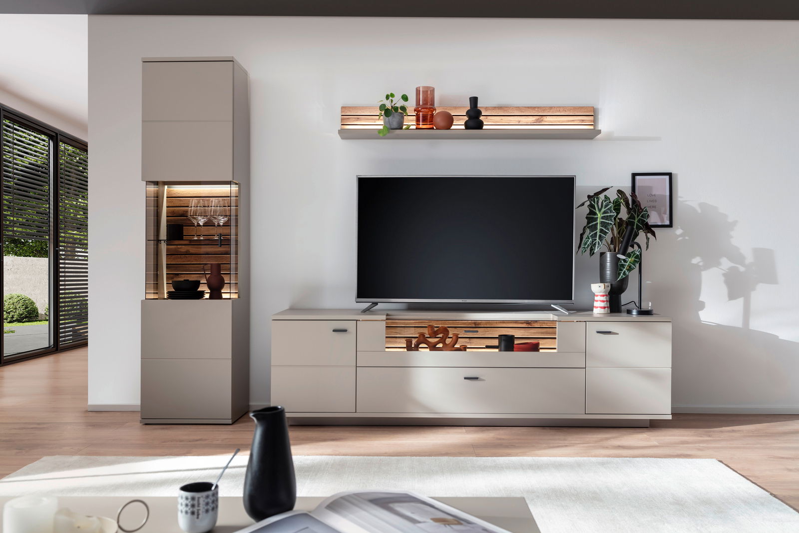 Moderne Wandkombination mit TV-Schrank, Vitrine und Regal in einem hellen Wohnzimmer, frontal betrachtet.