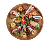 Vogelperspektive auf einen runden Snackteller aus Akazienholz, dekoriert mit Meeresfrüchten, Gemüse und essbaren Blüten.