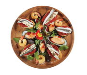 Vogelperspektive auf einen runden Snackteller aus Akazienholz, dekoriert mit Meeresfrüchten, Gemüse und essbaren Blüten.