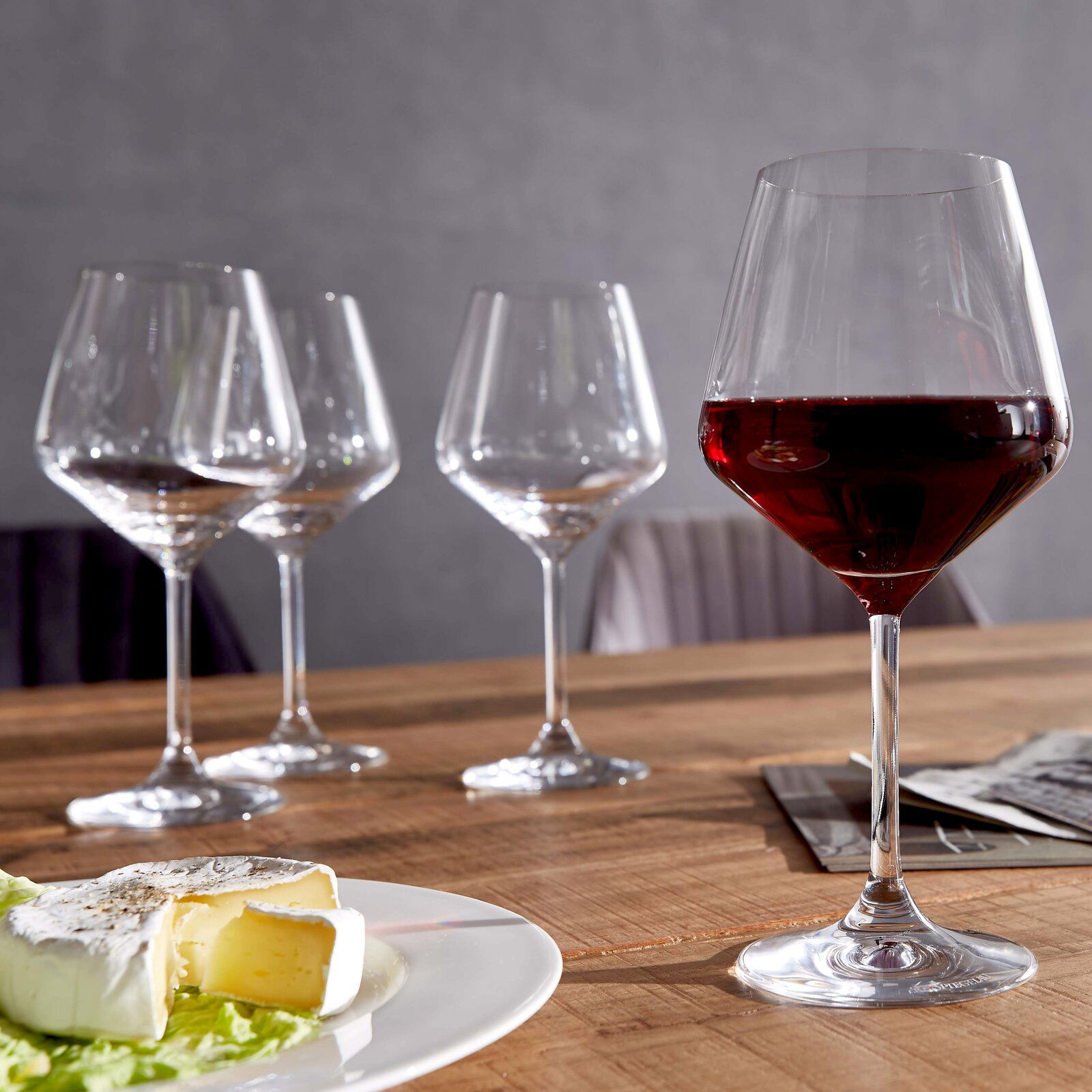 Spiegelau Burgundergläser-Style 4-tlg. Vier Burgundergläser auf einem Holztisch, eines gefüllt mit Rotwein, im Vordergrund ein Teller mit Käse. Perspektive: seitlich.