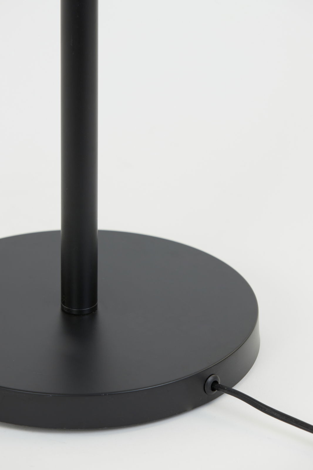 Nahaufnahme des schwarzen Sockels einer Stehleuchte mit Kabelanschluss, seitliche Perspektive.