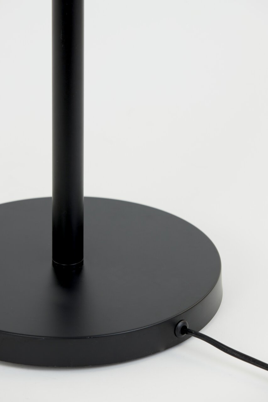Close-up van de zwarte voet van een staande lamp met kabelaansluiting, gezien vanaf de zijkant.