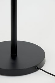 Close-up van de zwarte voet van een staande lamp met kabelaansluiting, gezien vanaf de zijkant.