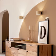 Moderne Wandleuchten in zylindrischer Form mit warmem Up-and-Down-Licht über einem Holz-Sideboard, fotografiert aus leicht seitlicher Perspektive (Halbprofil) im Wohnraum.