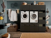 Moderne Hauswirtschaftsraum-Kombination mit Waschmaschine und Trockner, umgeben von Schränken und Regalen, frontal betrachtet.